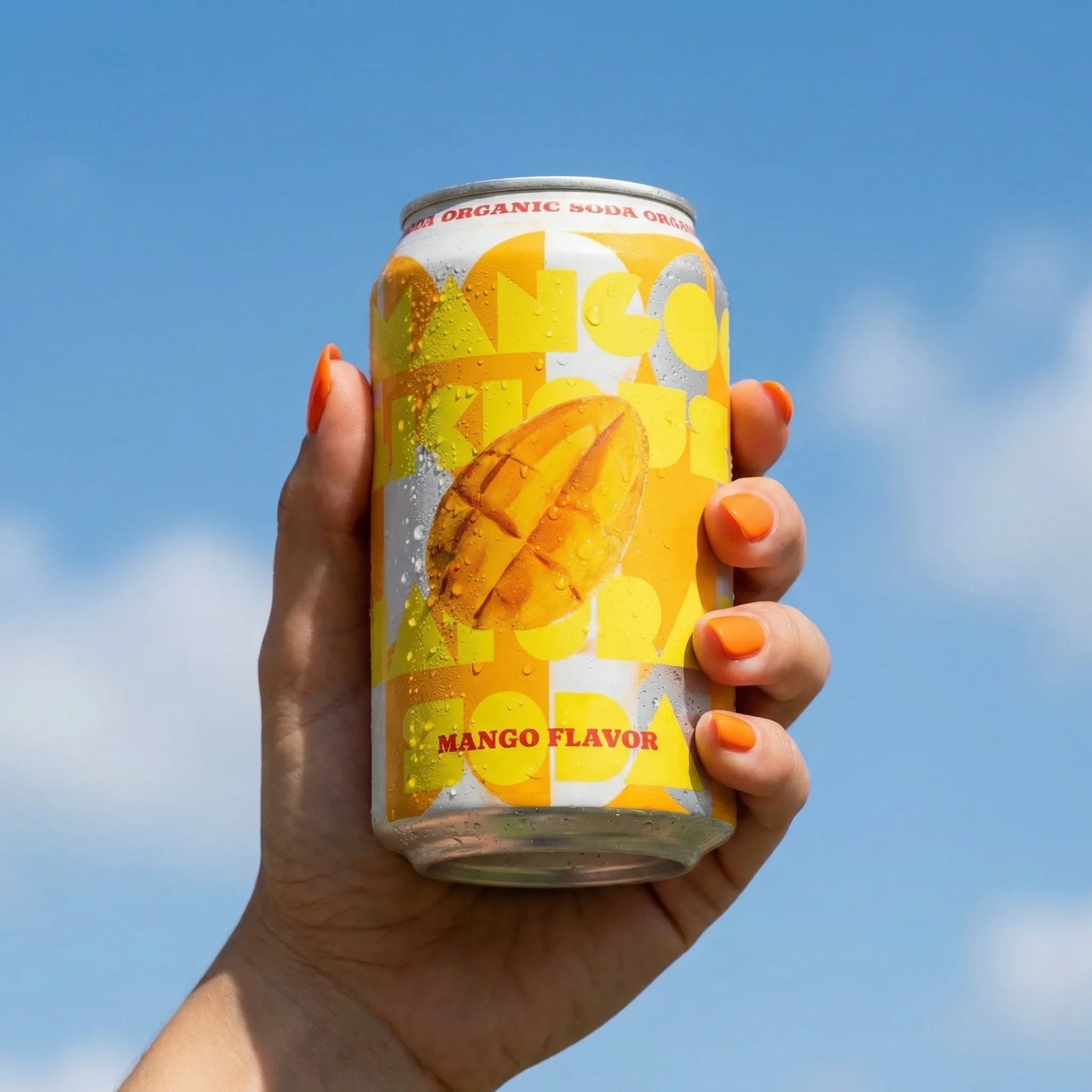 A canned drink held in a hand against a blue sky.