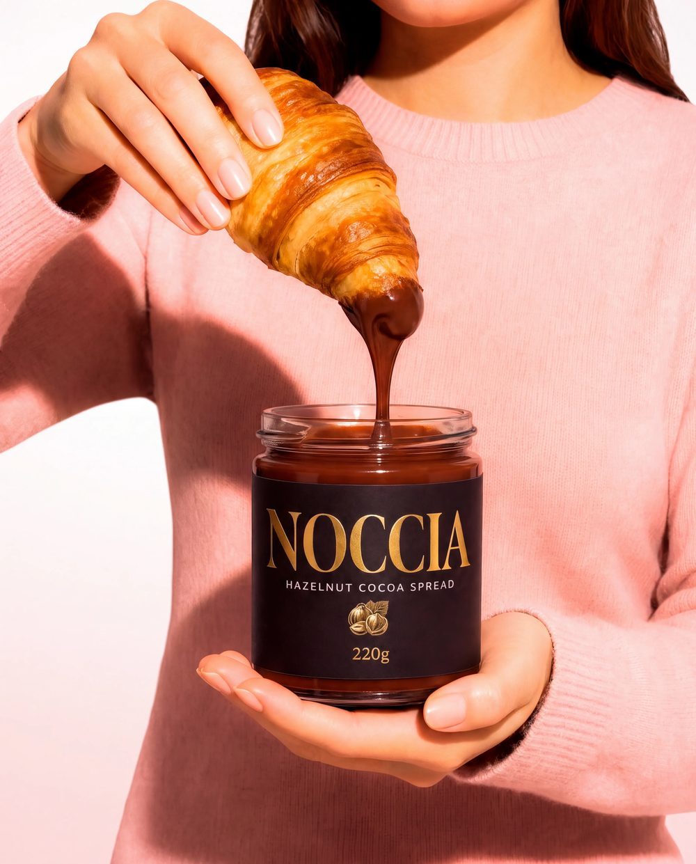 Croissant dipped into an open NOCCIA jar against a pink background