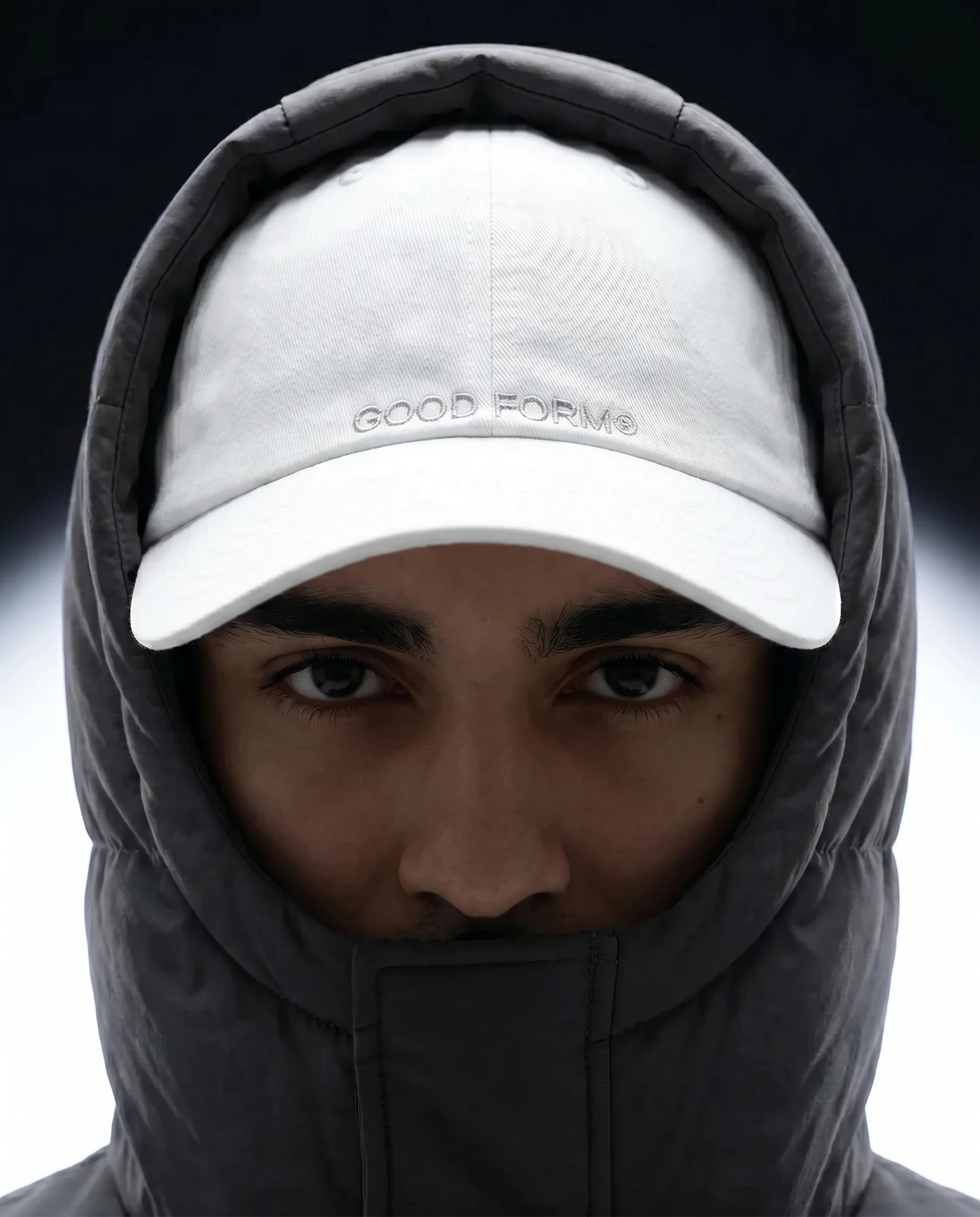 Close-up portrait of a model wearing a white performance cap and dark hood