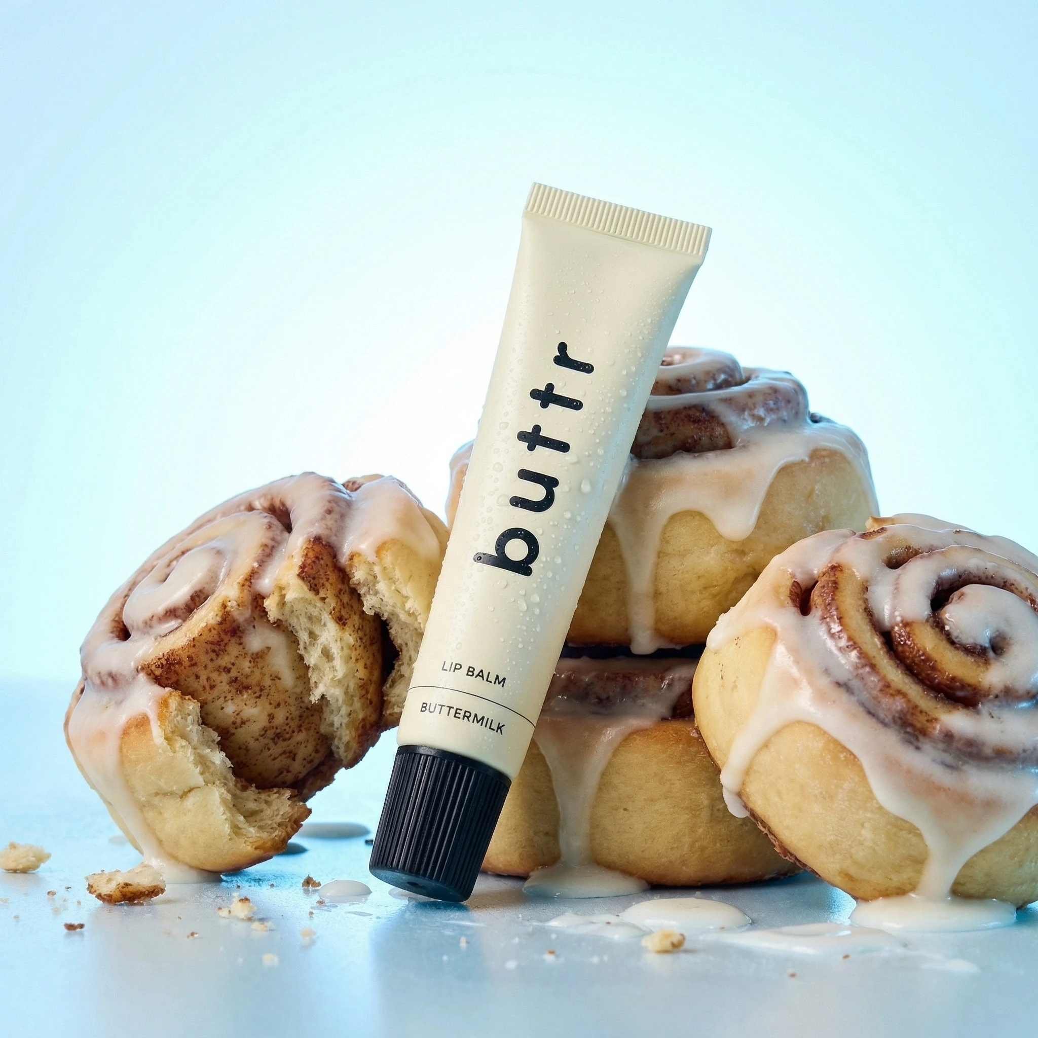 Lip balm tube styled with cinnamon buns against a blue background