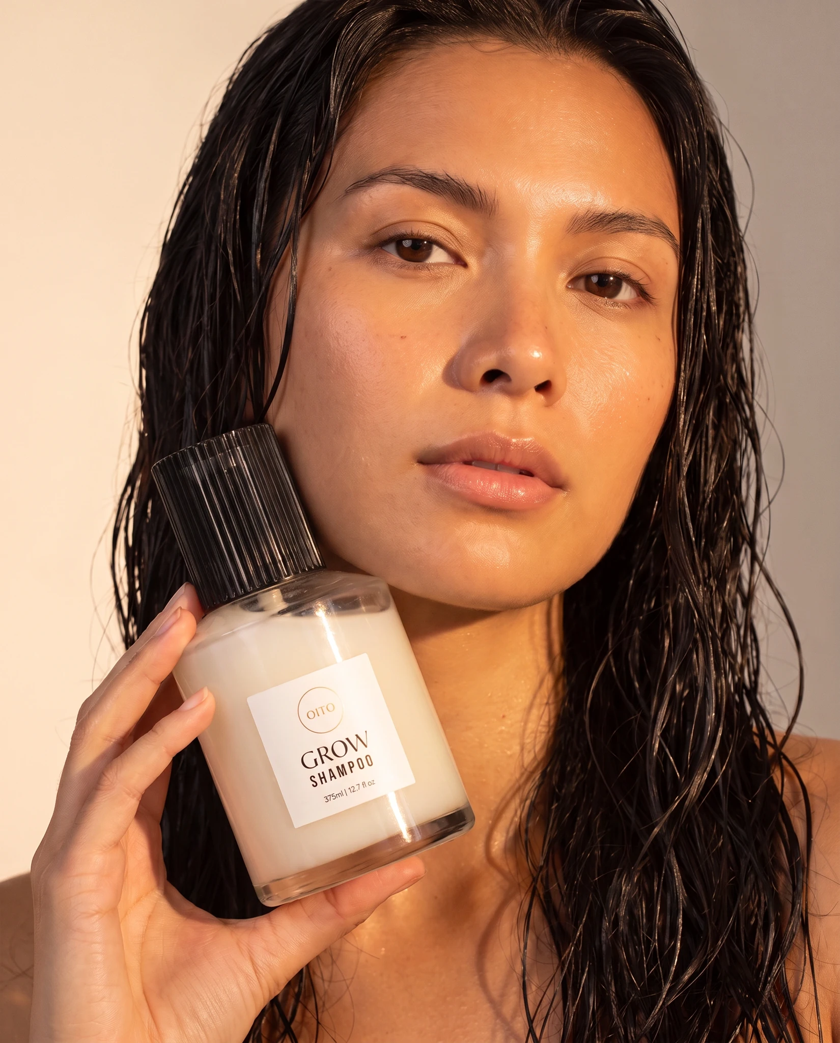 Model holding an OiTO Grow Shampoo bottle in a sunlit beauty portrait