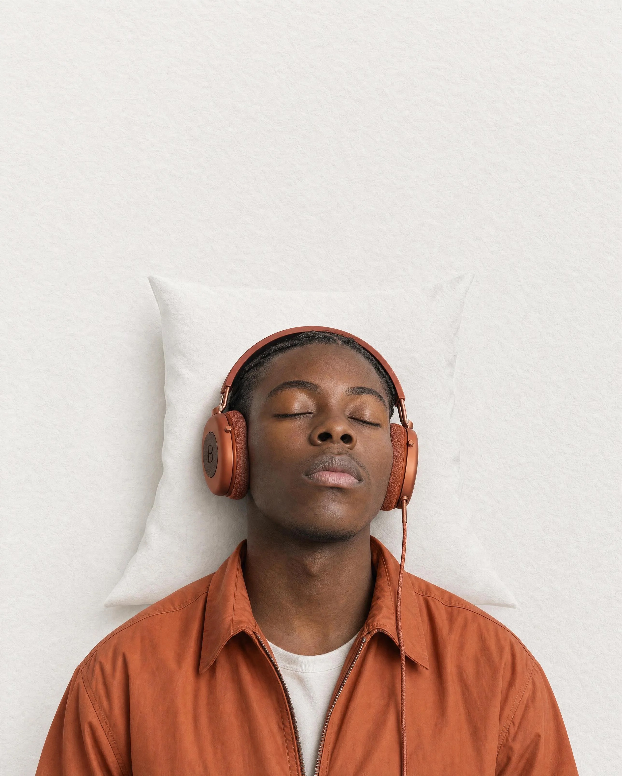 Man resting against a paper-textured pillow while wearing terracotta BOOM headphones