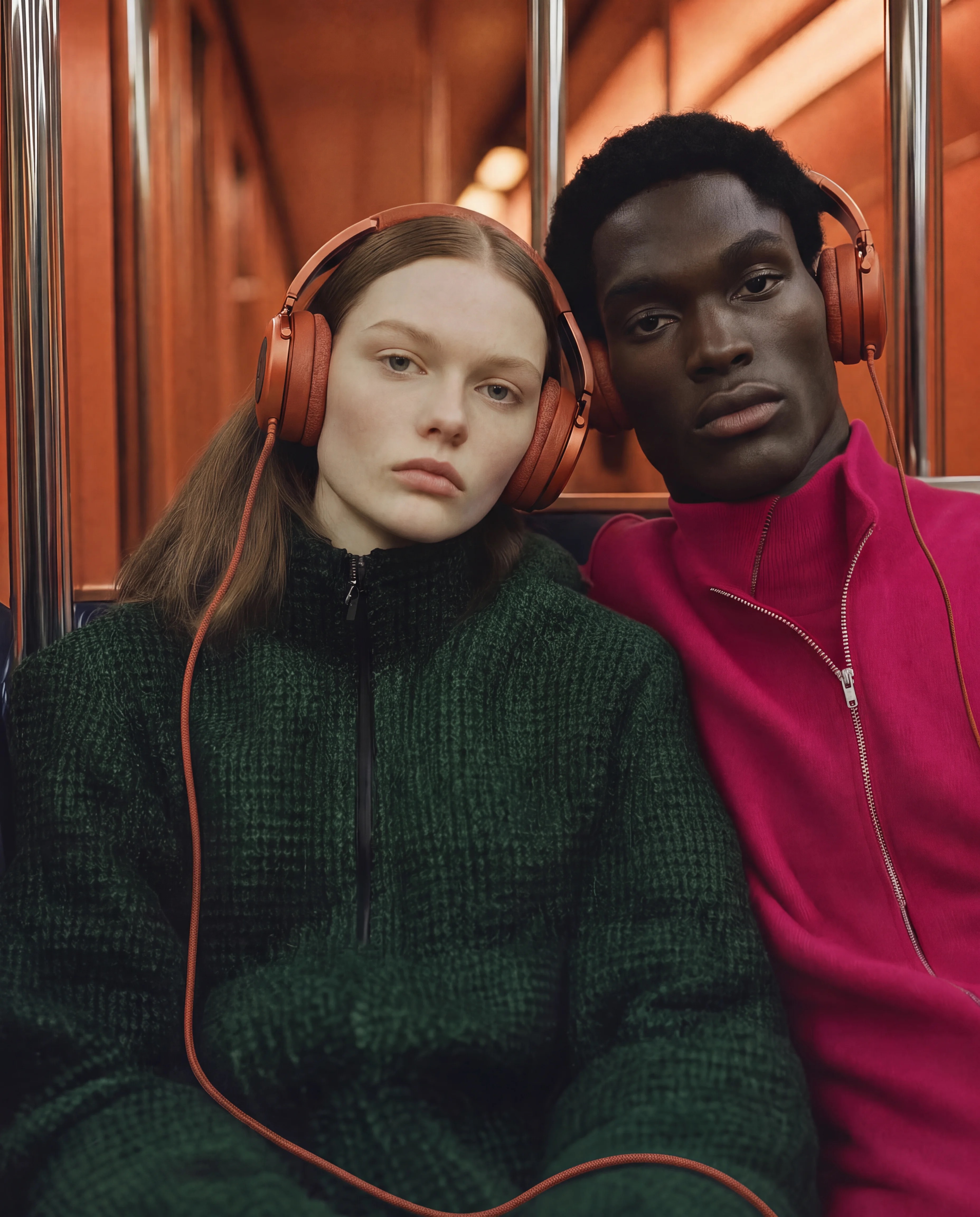 Two people wearing terracotta BOOM headphones in a warm subway car