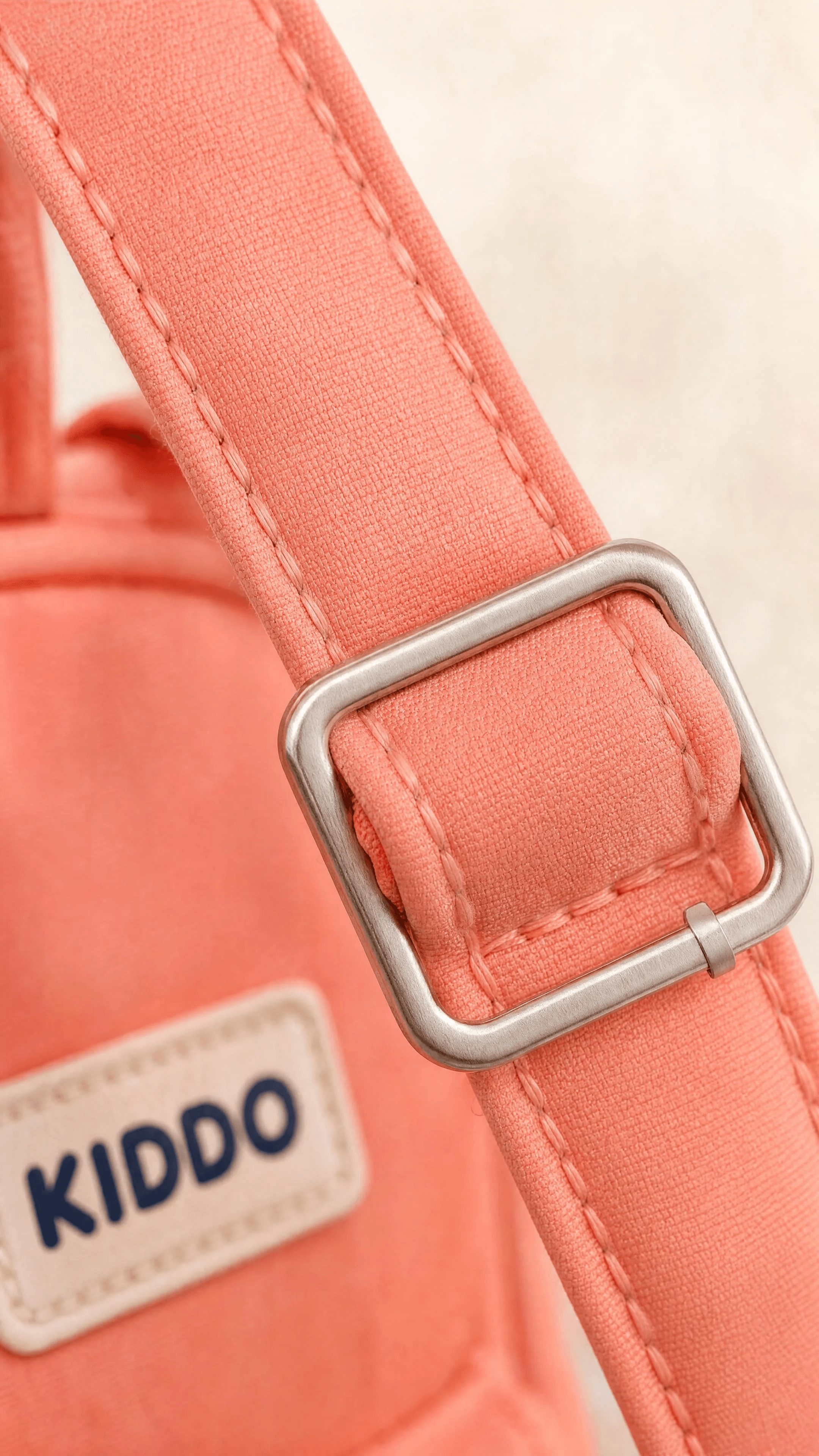 Coral nylon, bar-tacked stitching, and brushed-silver buckle hardware in extreme close-up.
