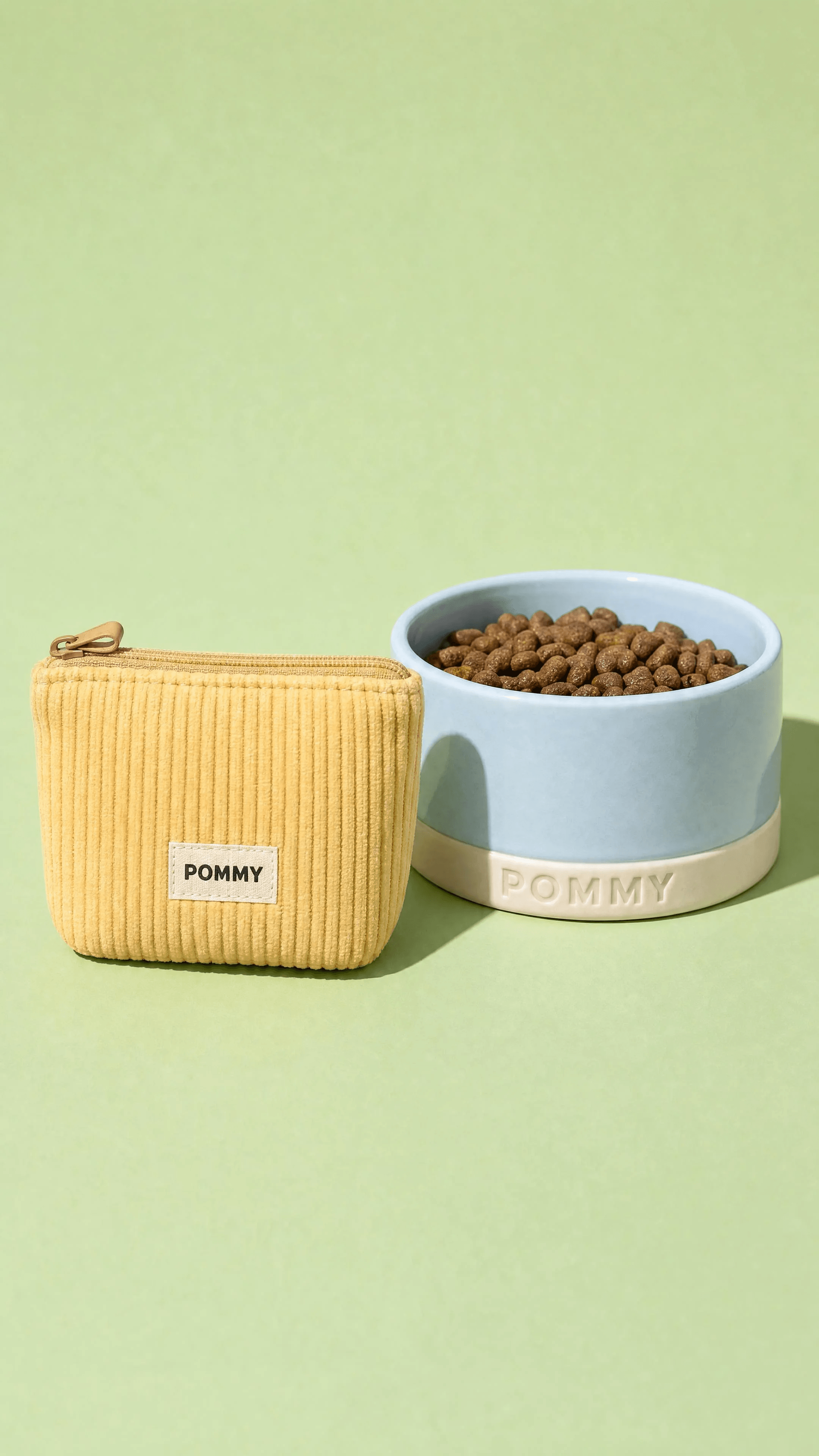 Butter-yellow POMMY treat pouch beside a sky-blue ceramic dog bowl