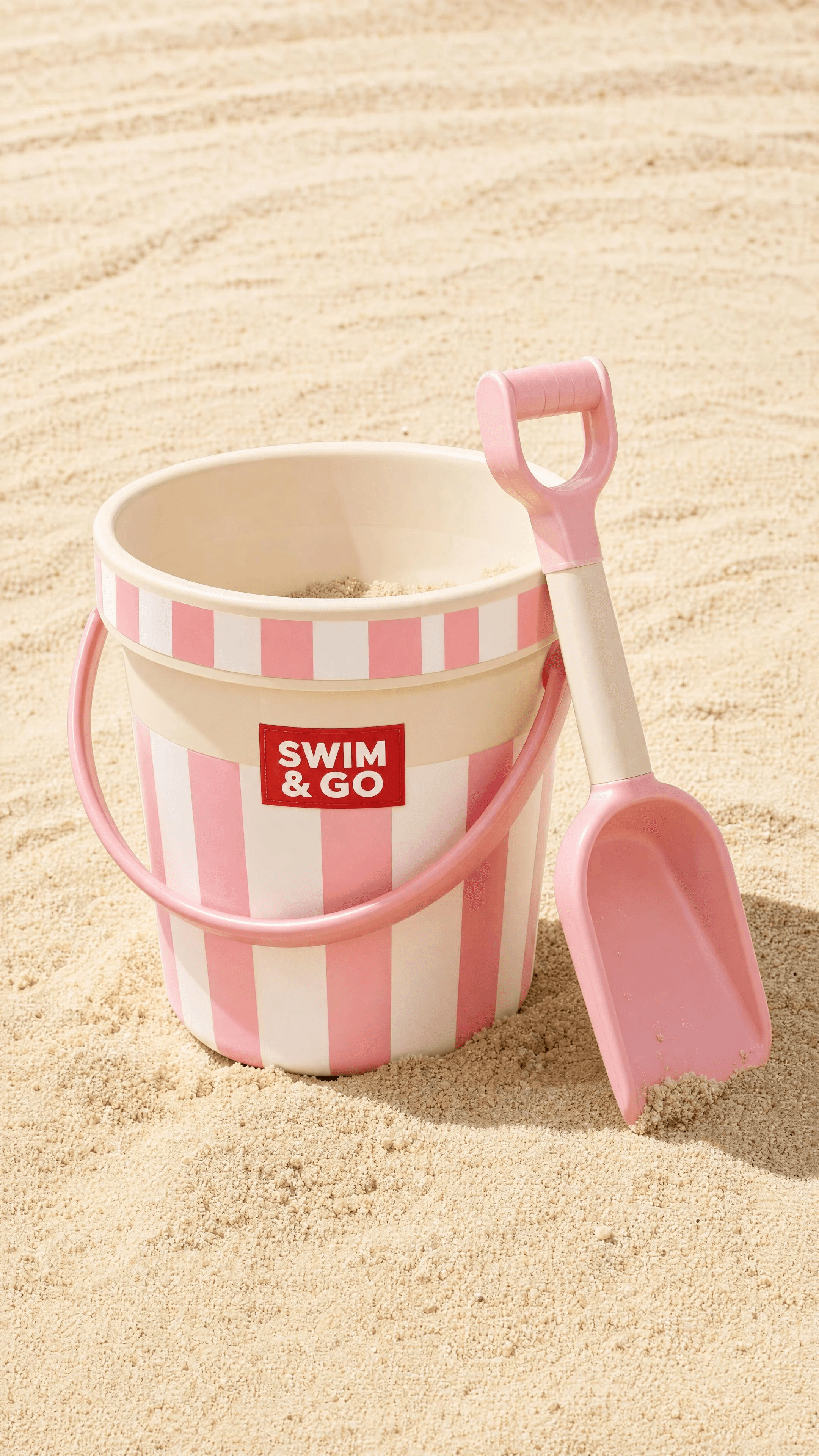 Pink-striped SWIM & GO beach bucket and shovel on sand