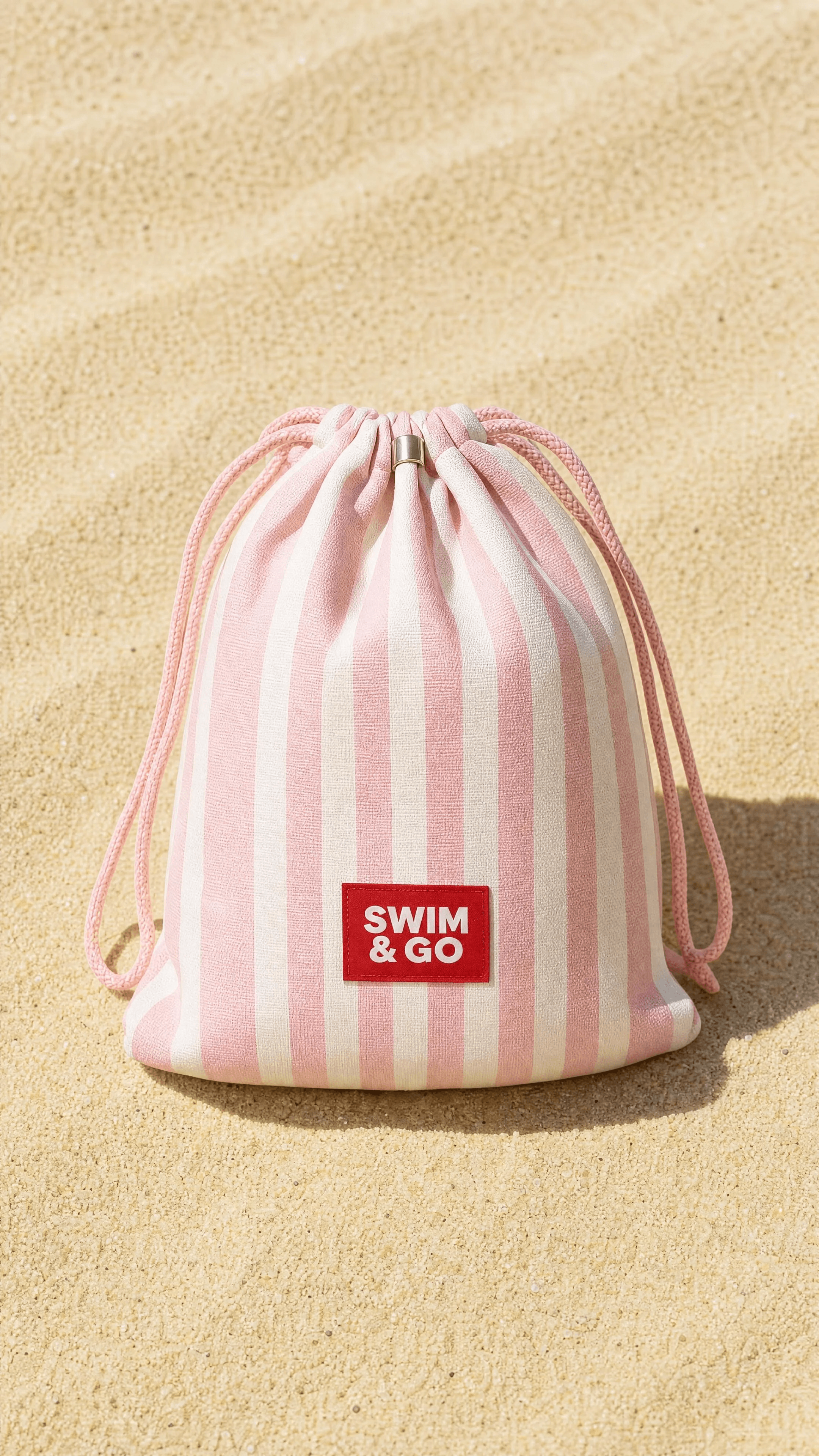 Pink-striped SWIM & GO drawstring beach pouch on sand