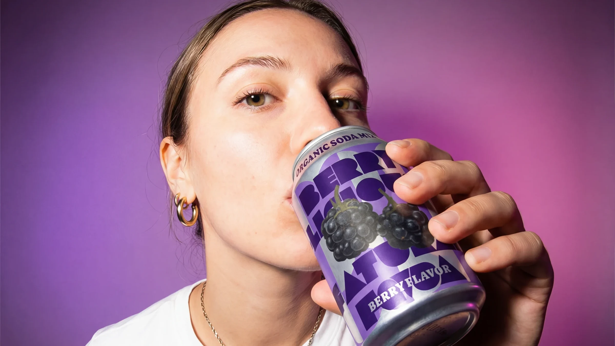 Person drinking a Berry Riot can against a purple and pink background